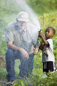 Community gardener John Doran has help from Zorte Edo, 3, watering a patch of vegetables. Zorte's father Keniabarido also gardens at the Antelope Community Garden.(William Lauer)